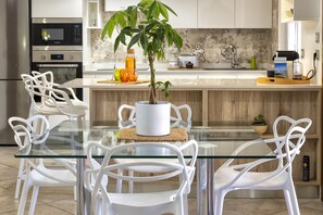 Uma cozinha moderna com armários brancos, uma mesa de jantar com tampo de vidro e cadeiras brancas.