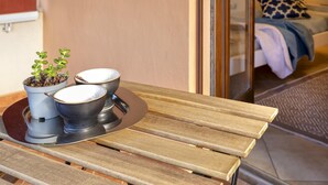 A wooden table with two potted plants and two bowls, a bed with a patterned pillow, and a patterned rug. - Sardinia Re - White Olives (Alghero)