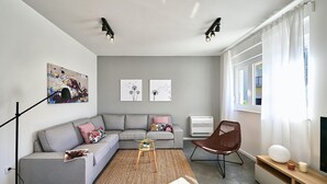 Un salon moderne avec un canapé gris, un fauteuil marron, une petite table et des œuvres d’art accrochées aux murs.