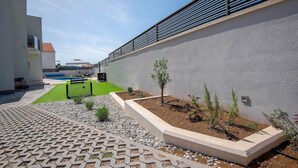 Un espace extérieur moderne doté d’une piscine, d’un petit jardin avec de jeunes arbres et d’un chemin pavé.