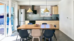 Une cuisine moderne avec une table à manger en bois, des chaises noires et beige, et des luminaires suspendus.