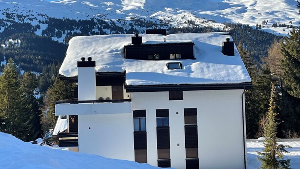 A modern two-story building with a snow-covered roof, surrounded by a mountainous landscape.