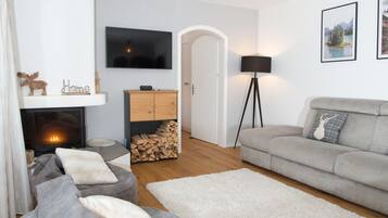 Un soggiorno moderno con camino, divani grigi, un tappeto bianco e una TV a parete.