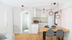 A modern kitchen with white cabinets, a wooden dining table, and two chairs. There is a small island with a sink and a kettle.