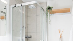 A modern bathroom with a glass-enclosed shower, a wooden vanity, a white sink, and a toilet.