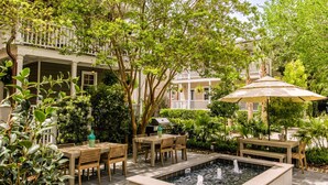 An outdoor patio with a rectangular water feature, wooden tables and chairs, and lush greenery. - 6C at Saint Philip Square, One Block to King, Classic Charleston Comfort (Charleston)