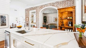 A modern kitchen with a marble island, a brick accent wall, and a wooden cabinet. - 6A at Saint Philip Square, One Block to King, Classic Charleston Comfort (Charleston)
