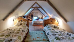 Ein gemütliches Schlafzimmer im Dachgeschoss mit zwei Einzelbetten, einer Holzleiter und einer geneigten Decke.