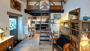 Ein gemütliches Zimmer mit einem Schlafpodest, einer Essecke mit Stühlen, einer Leiter und einem Bücherregal voller Bücher und Dekoration.