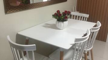 A dining area with a white table and chairs, a vase with red flowers, and a mirror on the wall.