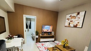 A modern living room with a sofa, coffee table, TV, and a dining area with a table and chairs. - Brenthill Condominium (Baguio)