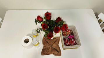 A table with a bouquet of red roses, a brown cloth bow, a small box of red items, and two bottles of liquid.