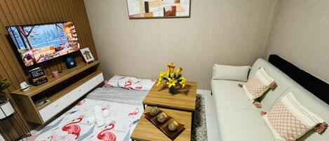 Un salon comprenant un canapé, une table basse agrémentée d’objets décoratifs, un téléviseur posé sur un meuble en bois et un tapis à motifs.