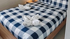 A hotel room with a checkered bedspread, a wooden headboard, a wall-mounted air conditioner, and a floral wallpaper pattern. - Brenthill Condominium (Baguio)