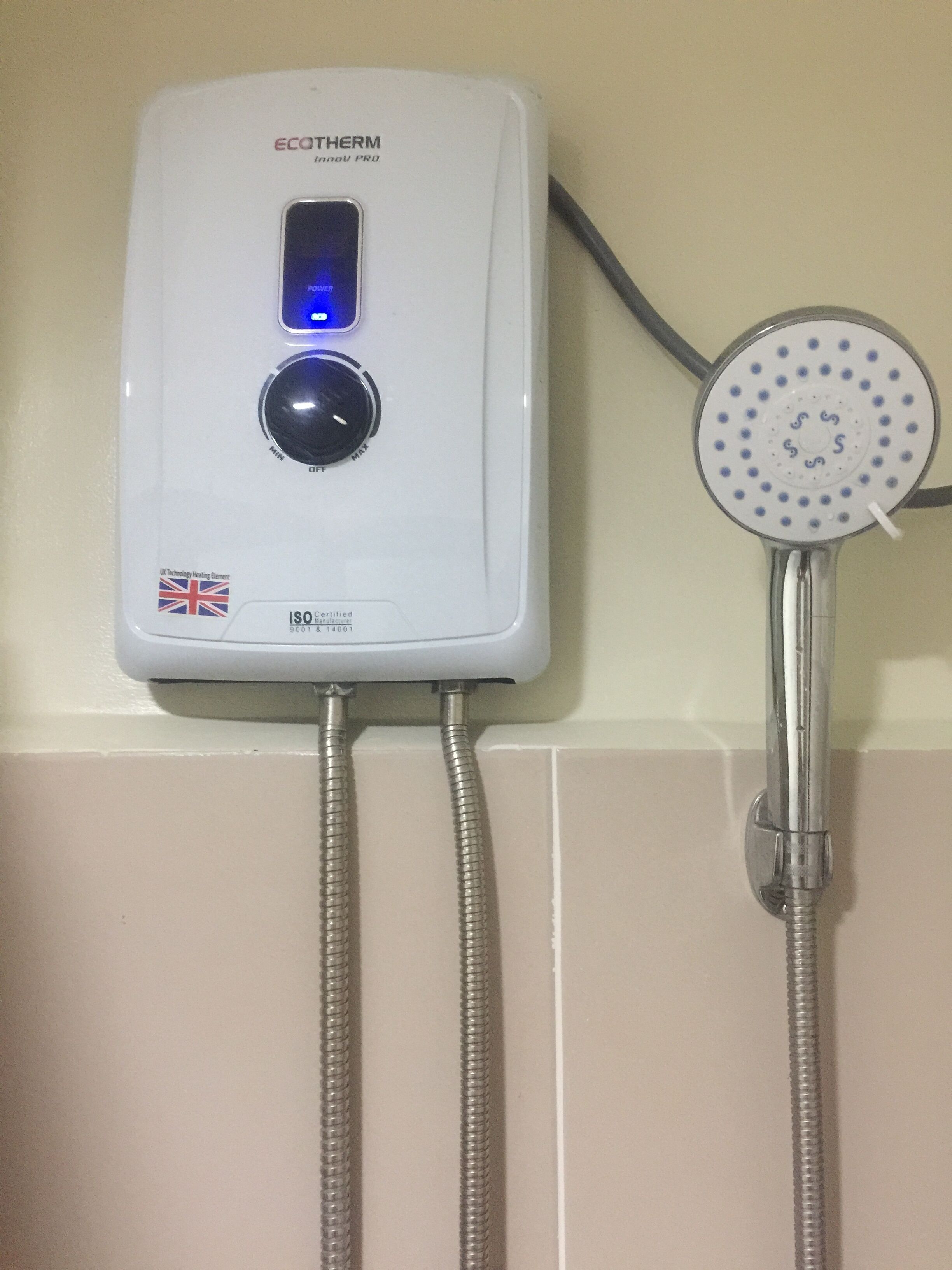 A white ECOTHEM InnovPro water heater with a digital display and two flexible hoses, connected to a showerhead.