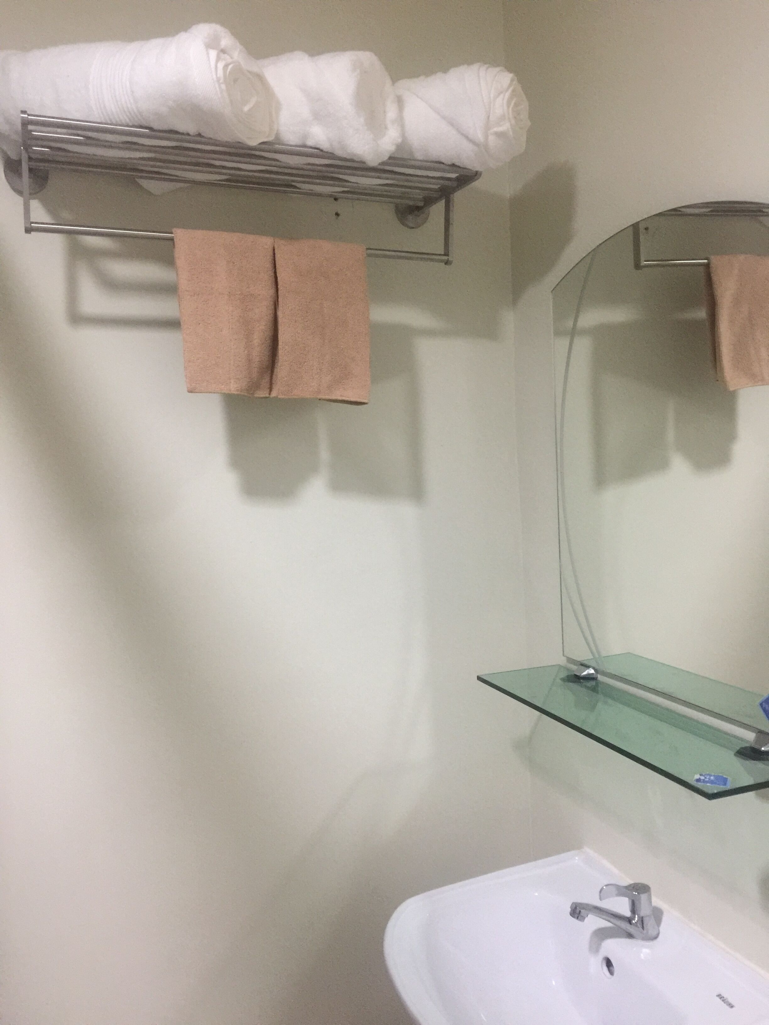 Ein Badezimmer mit einem weißen Waschbecken, einer Glasablage, einem Handtuchhalter mit weißen und braunen Handtüchern und einem Spiegel.