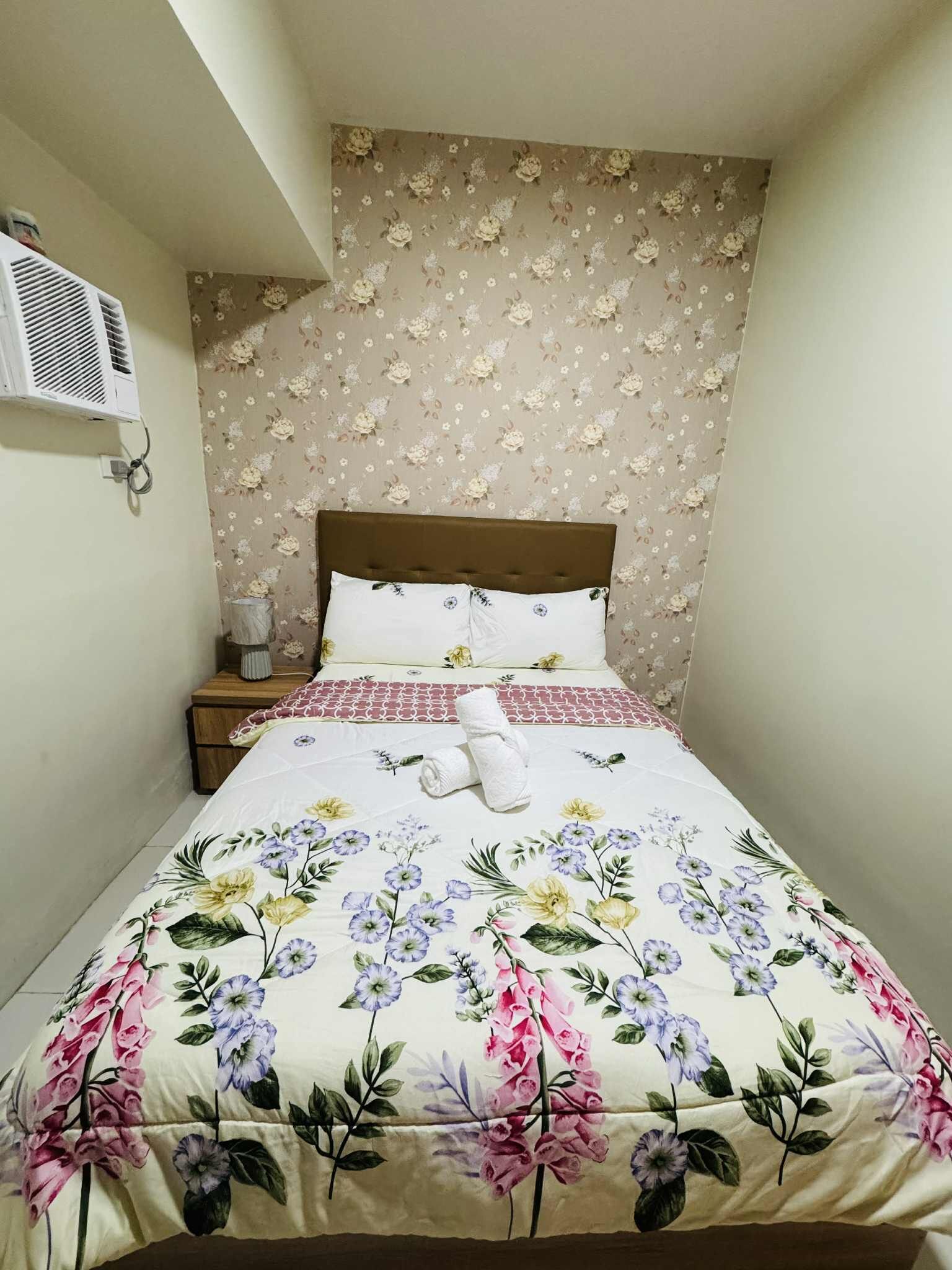 A neatly made bed with floral bedding, a wooden headboard, and a nightstand with a lamp.