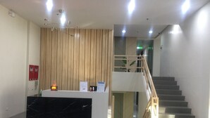A reception area with a black marble counter, wooden slatted wall, and a staircase with wooden railings. - Brenthill Condominium (Baguio)