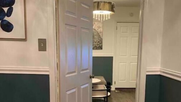 A hallway with a door leading to a room with a bed and a chandelier.