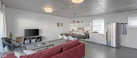 Un espacio habitable moderno con sofá, mesa de comedor, zona de cocina y televisor de pantalla plana.