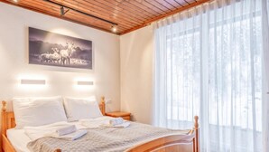 Un letto di legno con copriletto trapuntato, due comodini, una lampada a parete e un'ampia finestra con tende leggere.