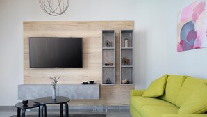 A modern living room with a flat-screen TV mounted on a wooden wall, a grey sofa, a small round table with a vase, and a grey rug.