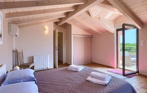 A bedroom with a large bed, a walk-in closet, and a sliding glass door leading to a balcony.