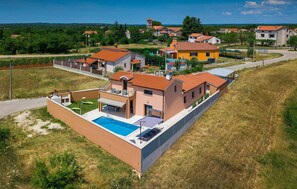 A modern villa with a swimming pool, a covered patio, and a view of the surrounding neighborhood.