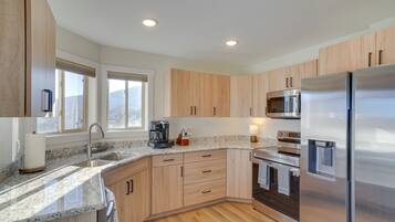 A modern kitchen with wooden cabinets, stainless steel appliances, a granite countertop, and a window providing a view of the outdoors.
