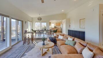 A spacious living area with a large window, a ceiling fan, a dining table, and a cozy seating area.