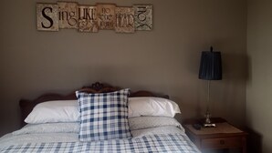 A bedroom with a bed, pillows, a wall-mounted sign, a nightstand, and a lamp. - Loess Hills Inn B&B (North Sioux City)
