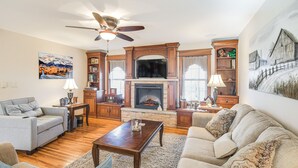 A living room with a fireplace, wooden bookshelves, a ceiling fan, and a large painting on the wall. - Charming Manchester Retreat w/ Patio & Fireplace! (Manchester)