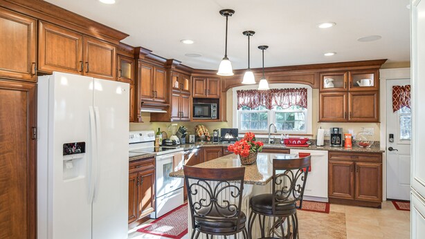A kitchen with wooden cabinets, a white refrigerator, a microwave, and a large island with bar stools. - Charming Manchester Retreat w/ Patio & Fireplace! (Manchester)