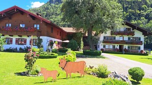 Un chalet tradizionale con un giardino, un vialetto lastricato e uno sfondo montano.
