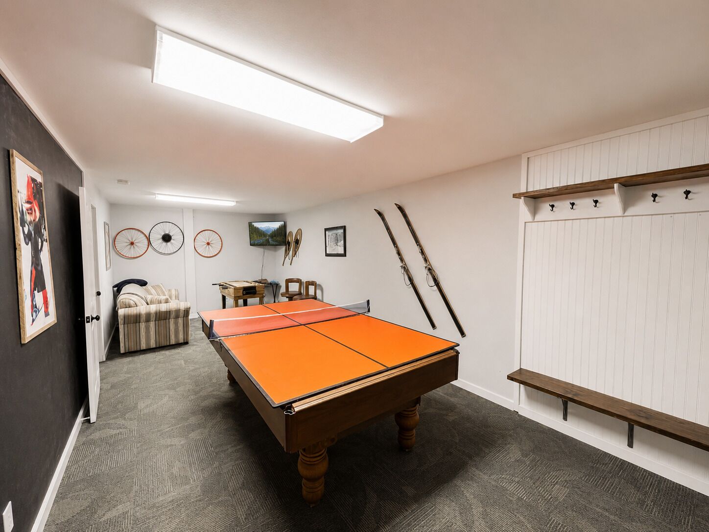 A billiards table in a room with a carpeted floor, a television, and wall-mounted skis.