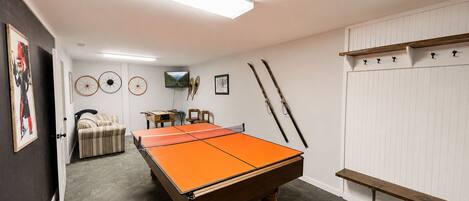 A billiards table in a room with a carpeted floor, a television, and wall-mounted skis.