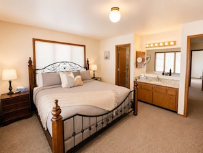 A bedroom with a four-poster bed, a vanity with a mirror, and a door leading to another room. - Mountain Cabin with Full Game Room (Durango)
