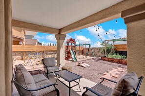 Un patio couvert avec des sièges extérieurs, une aire de jeux pour enfants et une vue dégagée sur le ciel.