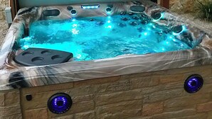 Un bain à remous avec un mur de pierres en arrière-plan, un banc en bois et deux commandes éclairées.