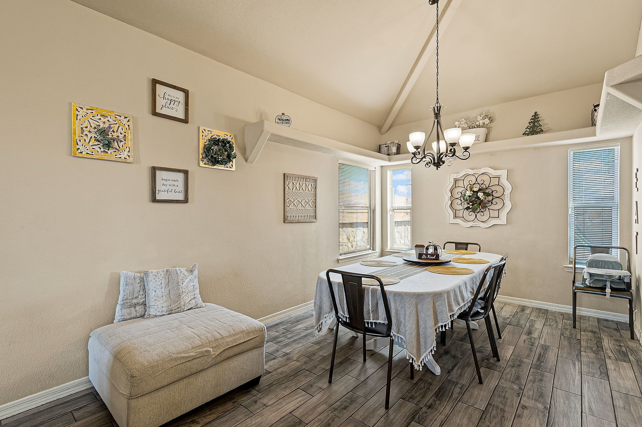 A dining area with a table set for four, surrounded by chairs, a sofa, and a decorative wall with framed artwork.