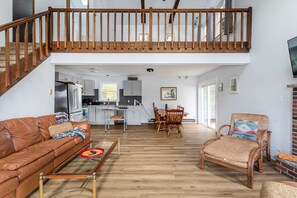 Un vaste espace de vie doté d’un haut plafond, d’un escalier en bois, d’une table à manger avec des chaises, d’un canapé en cuir et d’un fauteuil en osier.