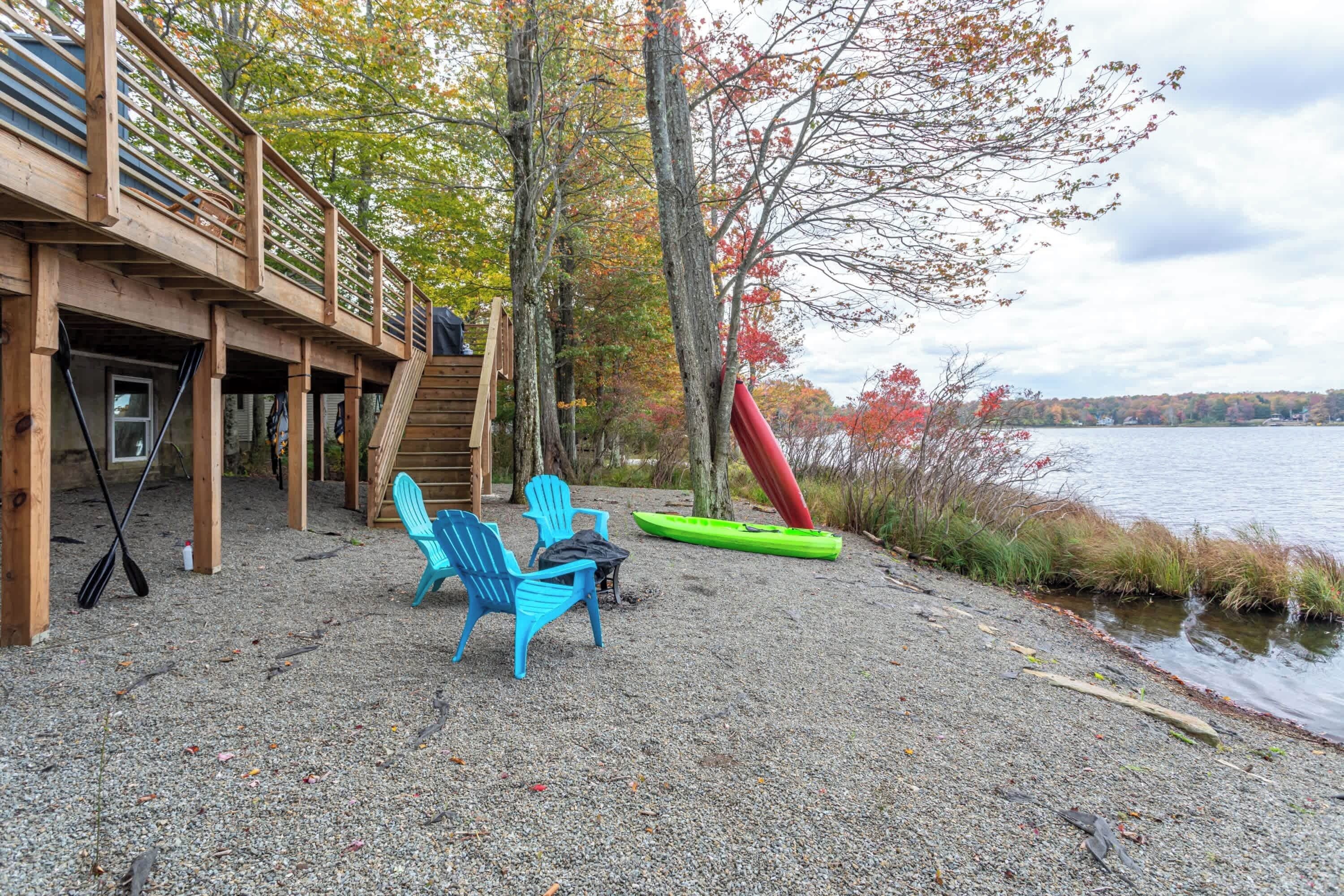 A wooden deck with chairs and kayaks by a lake.