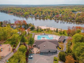 An aerial view of a lakeside property with a swimming pool, a parking lot, and surrounding trees. - Tranquil Shores | Waterfront | Fire Pit | Hammock (Tobyhanna)