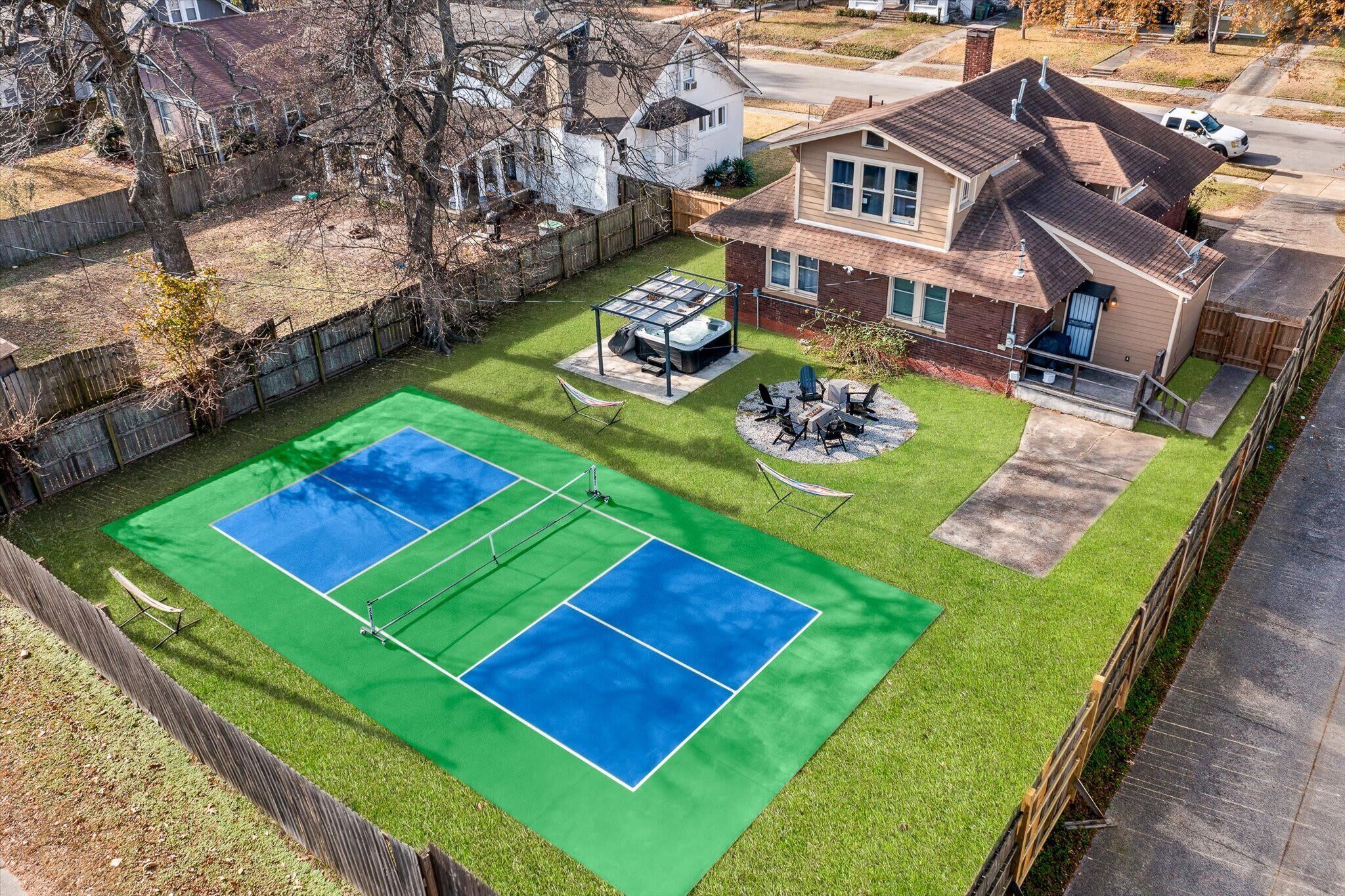 Ein Wohnhaus mit Tennisplatz, überdachter Terrasse und umzäunter Garten.