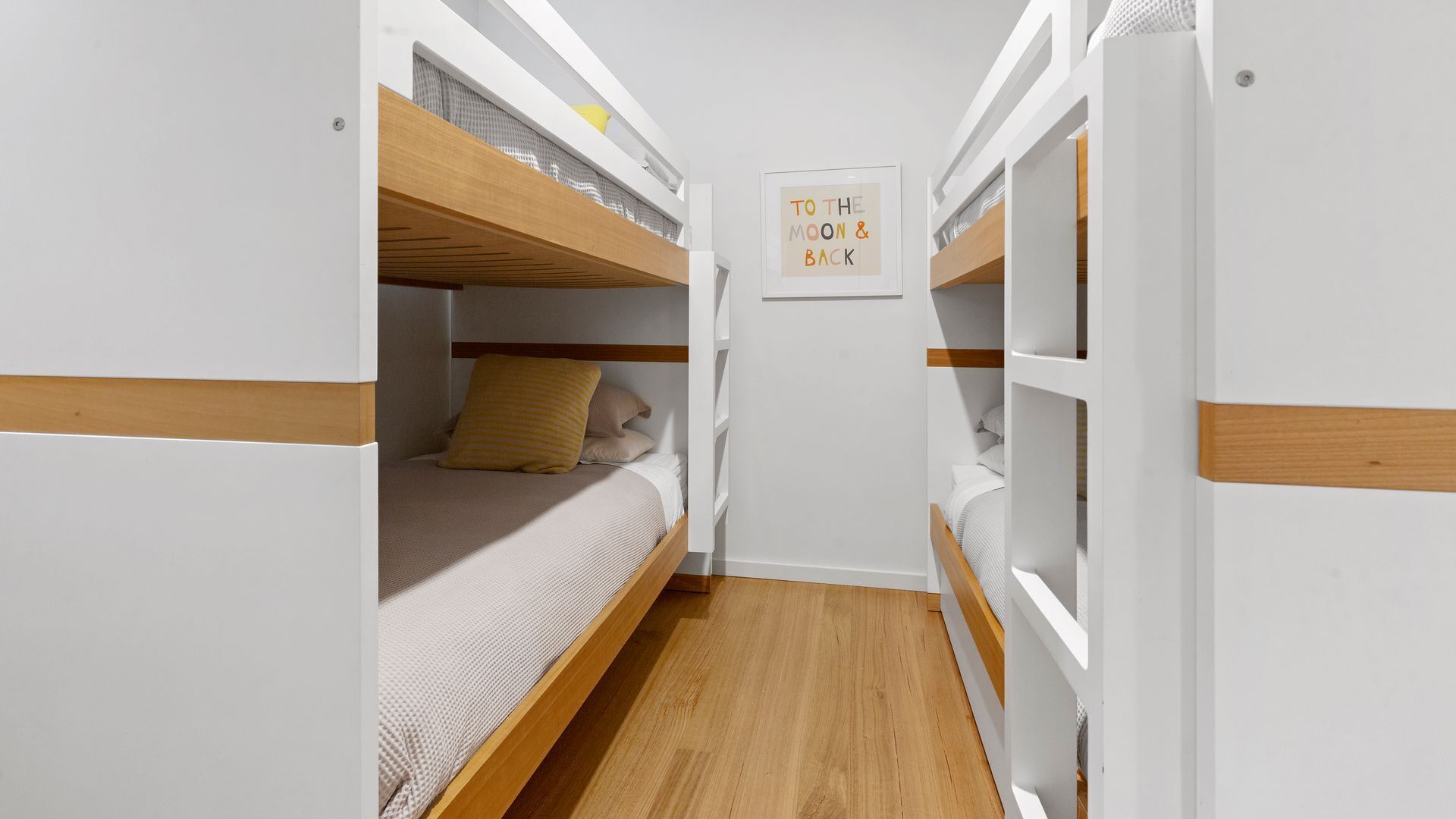 A narrow room with bunk beds, wooden flooring, and a framed sign on the wall.