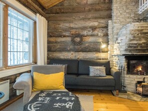 A cozy living room with a stone fireplace, a sofa with cushions, a rug, and a window with blinds.
