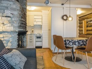 Hyggelig indretning med en stenvæg, spiseplads med et rundt bord og stole, samt et køkken med hvide skabe og en komfur.