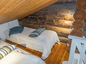 A cozy cabin with two beds, a wooden ceiling, and a log wall.