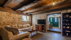 A cozy living room with a stone wall, a sofa, a TV, and a wooden cabinet. - Awesome home in Polaca (Polaca)