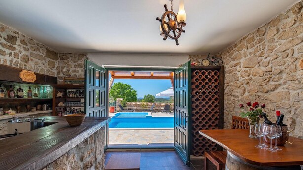 A bar area with a pool view, stone walls, and a wooden bar counter. - Awesome home in Polaca (Polaca)